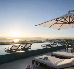 Piscina de borda infinita no rooftop ao amanhecer com espreguiçadeiras, guarda-sol e vista panorâmica para o mar e a cidade — Algae Beach Residence em Cachoeira do Bom Jesus, Florianópolis