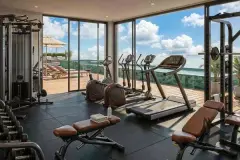 Academia equipada com esteiras, bicicleta elíptica, aparelhos de musculação e ampla janela com vista para a piscina e o mar — Almare Jurerê em Jurerê, Florianópolis