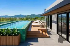Vista aérea real da piscina de borda infinita e deck de madeira com espreguiçadeiras e vista para os telhados e morros — Almare Jurerê em Jurerê, Florianópolis