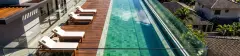 Piscina de borda infinita real com espreguiçadeiras, deck de madeira e cobertura com ripado ao fundo — Almare Jurerê em Jurerê, Florianópolis