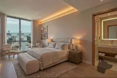 Fachada exterior do duplex vista da rua com pé direito duplo em vidro, pendentes esféricos e cozinha ao fundo — Almare Jurerê em Jurerê, Florianópolis