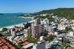 Vista aérea real do Apoena Studios inserido no centro de Jurerê Internacional com mar turquesa, praia, barcos e morros ao fundo — Apoena Studios em Jurerê, Florianópolis