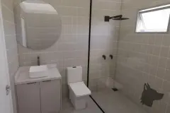 Perspectiva ilustrativa do banheiro com piso e paredes em azulejo claro, box de vidro com chuveiro e bancada suspensa — Aquamarina Residence em Cachoeira do Bom Jesus, Florianópolis