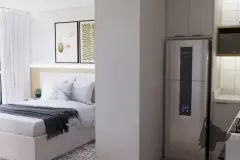 Perspectiva ilustrativa do dormitório com cama de casal e cozinha americana com geladeira ao lado, integração de ambientes — Aquamarina Residence em Cachoeira do Bom Jesus, Florianópolis