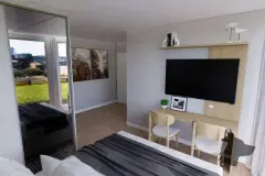 Perspectiva ilustrativa do dormitório com cama de casal, guarda-roupa espelhado, mesa de trabalho, cadeiras e TV — Aquamarina Residence em Cachoeira do Bom Jesus, Florianópolis