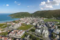 Vista aérea real do bairro Barra da Lagoa com praia, morros verdes, bairro consolidado e o Areias do Leste em destaque — Areias do Leste em Barra da Lagoa, Florianópolis