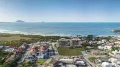 Vista aérea real do Areias do Leste com o mar azul, praia de areia, ilhas ao fundo e bairro ao redor — Areias do Leste em Barra da Lagoa, Florianópolis