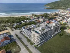 Vista aérea real do Areias do Leste em obras com rooftop e piscina visíveis, praia da Barra da Lagoa e morros ao fundo — Areias do Leste em Barra da Lagoa, Florianópolis