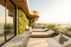 Foto real da varanda de cobertura com espreguiçadeiras de madeira, jardim vertical, sofás e vista ampla para o mar ao entardecer — Art Blue View em Jurerê, Florianópolis