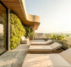 Foto real da varanda de cobertura com jardim vertical exuberante, espreguiçadeiras e sofás, estrutura curva em concreto e vista para o mar — Art Blue View em Jurerê, Florianópolis