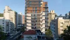 Foto real da fachada do Art Places ao amanhecer, torre de 14 andares com sacadas salientes, revestimento de madeira no topo e rua do Centro de Florianópolis — Art Places em Centro, Florianópolis