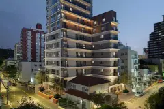 Foto real da fachada do Art Places à noite com iluminação nas lajes e revestimento de madeira nos andares superiores no Centro de Florianópolis — Art Places em Centro, Florianópolis