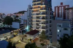Foto real da fachada do Art Places ao entardecer com iluminação nas lajes, torre de 14 andares inserida no entorno do Centro de Florianópolis — Art Places em Centro, Florianópolis