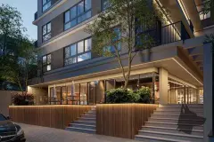 Perspectiva da entrada do Art Places iluminada à noite com café envidraçado, ripas de madeira, árvore e escadas de acesso — Art Places em Centro, Florianópolis