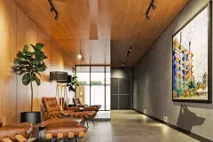 Perspectiva do lobby com poltronas de couro caramelo, teto revestido de madeira, planta ornamental ficus e obra de arte abstrata na parede de cimento — Arts Home Design em Ingleses, Florianópolis