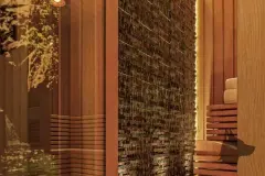 Perspectiva da sauna finlandesa com bancadas de cedro, parede de pedra bruta com iluminação dourada e reflexos de vegetação no vidro — Arts Home Design em Ingleses, Florianópolis