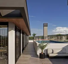 Perspectiva do terraço de lazer com piscina, passarela lateral, sofá externo e palmeira, visão alternativa com céu azul — Arts Home Design em Ingleses, Florianópolis