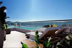 Perspectiva do rooftop com piscina de borda infinita, deck de madeira, espreguiçadeiras e vista para o mar de Jurerê — At One Jurerê Studios em Jurerê, Florianópolis