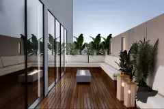 Perspectiva da varanda privativa com sofá em L branco, deck de madeira, luminária de bambu e plantas tropicais ao entardecer — At One Jurerê Studios em Jurerê, Florianópolis