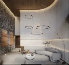 Perspectiva do lobby com pé-direito duplo, sofá orgânico cinza, parede de pedra natural e luminários circulares suspensos — Aura em Agronômica, Florianópolis
