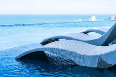 Foto de espreguiçadeiras de vime flutuando em piscina infinita com vista para o mar azul — Aurum Blue View em Jurerê, Florianópolis