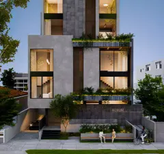Perspectiva da fachada frontal do edifício Aurum Blue View com jardins, entrada, banco externo e moradores ao entardecer — Aurum Blue View em Jurerê, Florianópolis