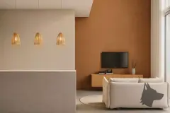 Perspectiva da sala de estar do apartamento do B7 Essence Brava com sofá bege, mesa de centro e parede accent terracota com TV — B7 Essence Brava em Praia Brava, Florianópolis