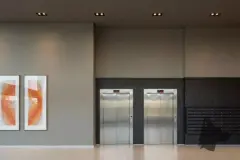 Perspectiva do hall com dois elevadores em aço inox, painéis de arte e caixas de correspondência — B7 Park Marina em Agronômica, Florianópolis