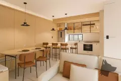 Sala de estar e jantar integrada à cozinha, decoração em madeira e tons caramelo, mesa redonda e bancada com bancos — Bella Sintra Residence em Estreito, Florianópolis