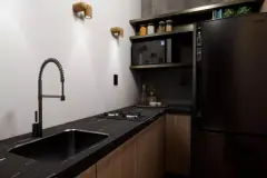 Cozinha compacta em L com bancada preta em mármore, fogão de indução e geladeira preta, arandelas de madeira — Beriyth Residence em Cachoeira do Bom Jesus, Florianópolis