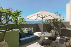 Terraço privativo com sofá azul, mesa redonda, guarda-sol e vista para as montanhas de Canasvieiras — BG Connect Canas em Canasvieiras, Florianópolis