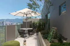 Terraço privativo menor com mesa redonda, cadeiras aramadas, guarda-sol, jardim e pug sentado — BG Connect Canas em Canasvieiras, Florianópolis
