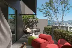 Varanda com poltronas vermelhas, mesa bistrô, vaso com frangipani e vista para a cidade e montanhas — BG Connect Canas em Canasvieiras, Florianópolis
