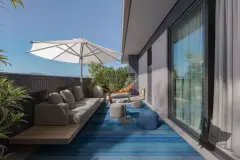 Terraço privativo com sofá, rede, mesa redonda, guarda-sol azul e tapete listrado — BG Connect Trindade 2 em Trindade, Florianópolis