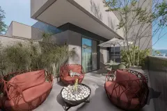 Terraço privativo com sofás terracota, fire pit com pedras brancas, mesa de jantar e guarda-sol — BG Connect Trindade 2 em Trindade, Florianópolis