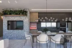 Sala de jantar e cozinha integrada, parede de pedra com TV, mesas e cadeiras brancas e pendente de esferas — Bohn Residence em Ingleses, Florianópolis
