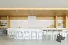 Perspectiva ilustrativa da cozinha gourmet com bancada branca longa, banquetas brancas e armários em madeira com parede neutra — D/Season Residence Club em João Paulo, Florianópolis