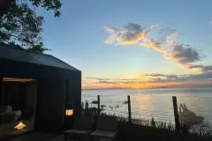Foto real do pôr do sol sobre a Baía Norte visto do terreno com estrutura escura e lanterna em primeiro plano — D/Season Residence Club em João Paulo, Florianópolis