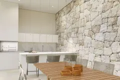 Perspectiva ilustrativa do espaço gourmet coberto com mesa de madeira, cadeiras de fibra e parede em pedra com bancada branca — D/Season Residence Club em João Paulo, Florianópolis