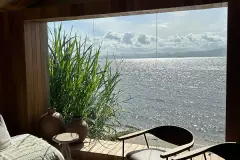 Foto real do interior do módulo de bem-estar com janela quadrada emoldurada em madeira com vista para a Baía Norte e plantas altas — D/Season Residence Club em João Paulo, Florianópolis