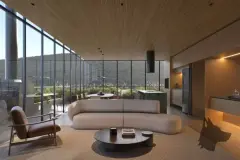 Perspectiva da sala de estar integrada à cozinha com sofá, ilha de mármore e banquetas, vista para a varanda com natureza — Dália em Canasvieiras, Florianópolis