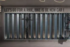 Perspectiva do bicicletário do Domus 544 com suportes metálicos e frase decorativa na parede — Domus 544 em Agronômica, Florianópolis