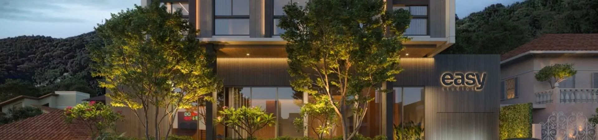 Fachada noturna do edifício Easy Studios com iluminação dourada, jardins e placa Easy na entrada com morros ao fundo — Easy Studios em Centro, Florianópolis