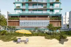 Fachada do edifício com revestimento verde-água e pastilhas teal, vista da praia com guarda-sol amarelo e cadeiras na areia — Gaivotas 4 em Ingleses, Florianópolis