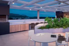Rooftop ao entardecer com mesa redonda branca, sofá, jardim suspenso, churrasqueira com armários de madeira e vista para os morros — Gran Malltech Business by Housi em Vargem Grande, Florianópolis