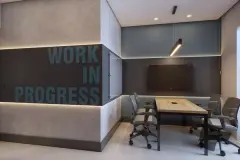 Sala de reuniões com mesa, cadeiras ergonômicas, TV e letreiro Work in Progress — HUB Beira Mar em Saco dos Limões, Florianópolis
