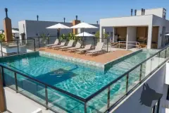 Piscina no rooftop com espreguiçadeiras e guarda-sol, deck de madeira e vista para o bairro — Icone Residence em Ingleses, Florianópolis