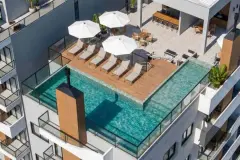 Vista aérea da piscina no rooftop com deck de madeira, espreguiçadeiras e guarda-sol — Icone Residence em Ingleses, Florianópolis