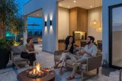 Área de convivência no rooftop à noite com lareira, sofás, cozinha gourmet e pendentes de palha iluminados — Icone Residence em Ingleses, Florianópolis