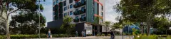 Fachada do empreendimento vista da rua, edifício de 9 andares com fachada verde, branca e vermelha, árvores ao redor e pedestres na calçada — Imob Trindade On em Trindade, Florianópolis